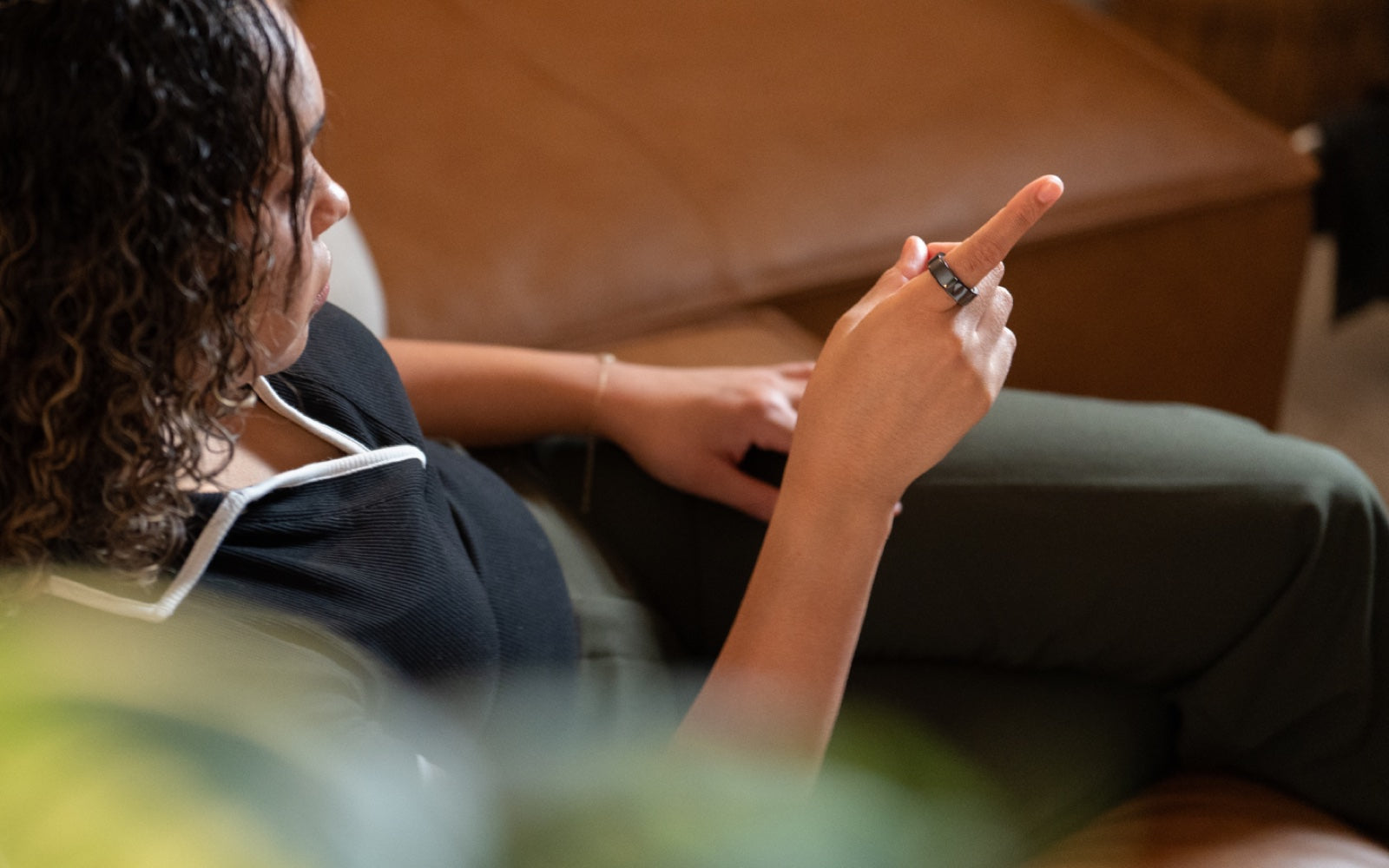 A woman relaxing on a sofa, pointing with the KiWear Ring on her finger